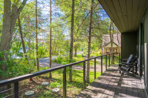 A balcony view overlooking a lush green landscape with trees and a cozy house in the distance.