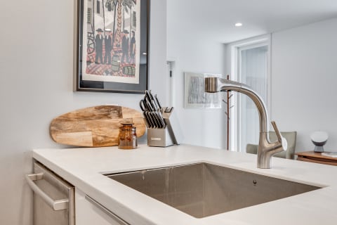 A modern kitchen countertop with a stainless steel sink, faucet, cutting board, and knife set.