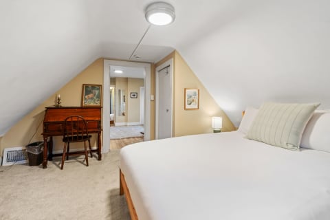 Cozy attic bedroom featuring sloped ceilings, a bed, writing desk, and charming decor.