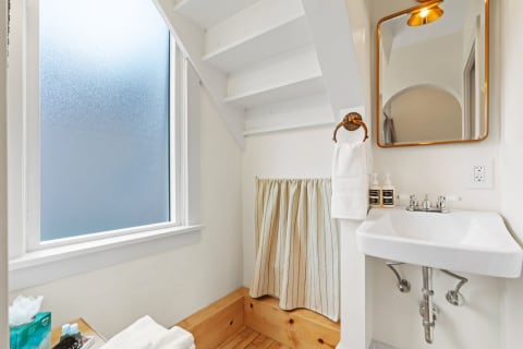 Compact bathroom with a frosted window, white sink, and wooden bench.