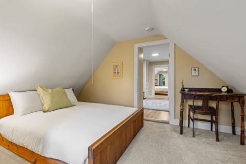 Cozy attic bedroom featuring a wooden bed, desk, and a view into another room.