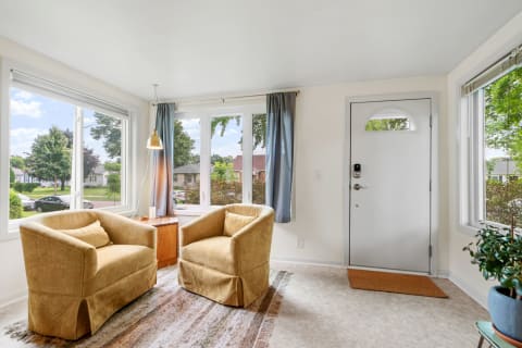 Bright sitting area featuring two armchairs, a side table, and a front door with windows beside it.