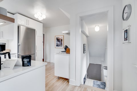 Bright modern kitchen with stainless steel refrigerator and wooden flooring, featuring a staircase in the background.