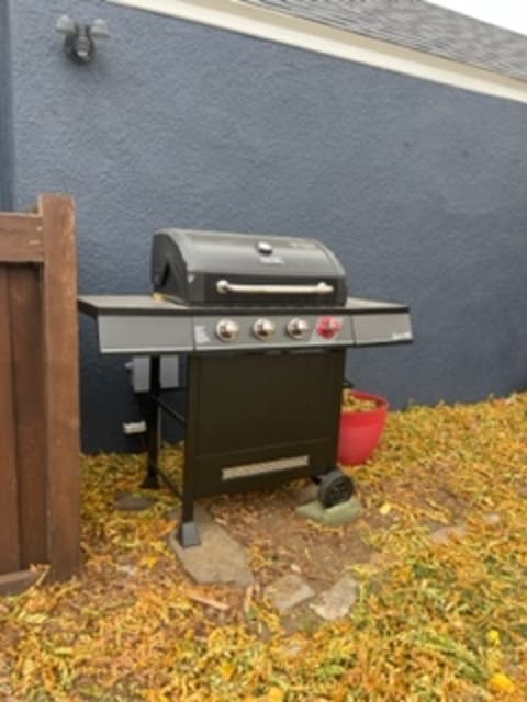 A black gas grill in a backyard with a gray wall and fallen leaves.