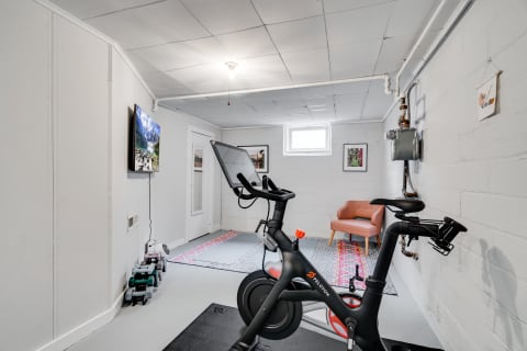 A basement room with a Peloton bike, weights, and an armchair.