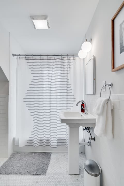A contemporary bathroom with a striped shower curtain, pedestal sink, and grey bath mat.