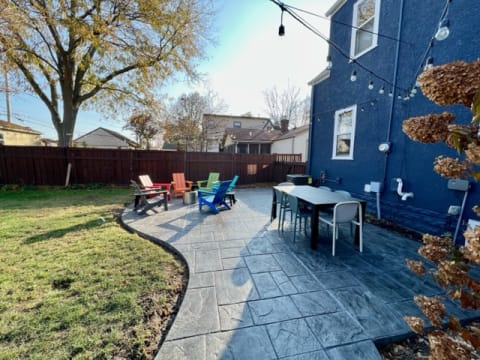 An outdoor patio with colorful chairs and a dining table surrounded by a lawn and trees.
