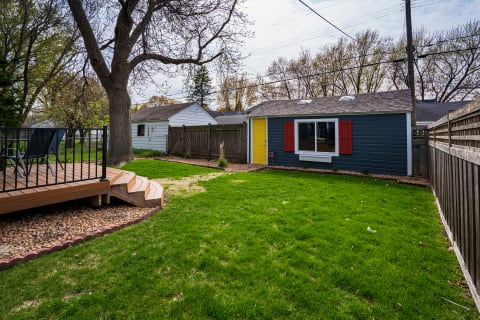 Backyard scene with a green lawn, a small blue building with red shutters, and a wooden deck.