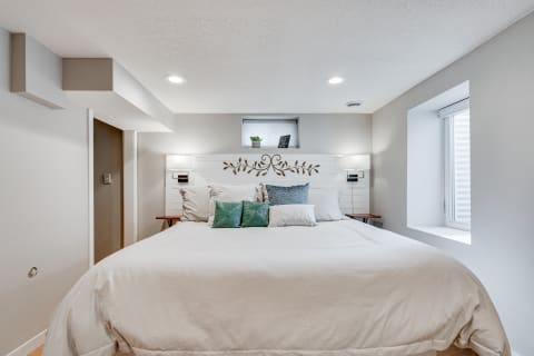 Modern bedroom with a white bed and decorative pillows, soft lighting, and a small window.