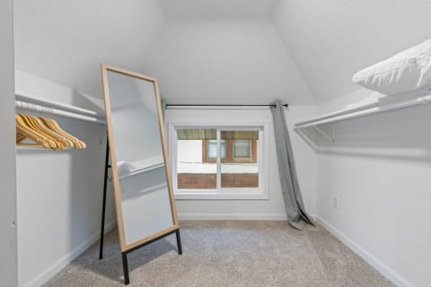 Interior view of a tidy attic-style closet with a mirror, hangers, and a window.