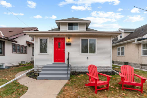 Exterior view of a house featuring a red door and two red Adirondack chairs.