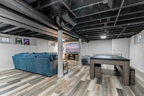 An inviting basement space featuring a blue sectional sofa, a game table, and a media console.