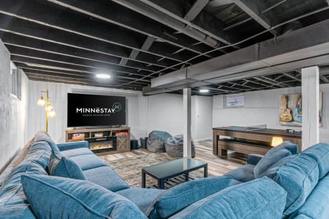A spacious and inviting basement recreation room featuring a blue sectional sofa, television, and ping-pong table.