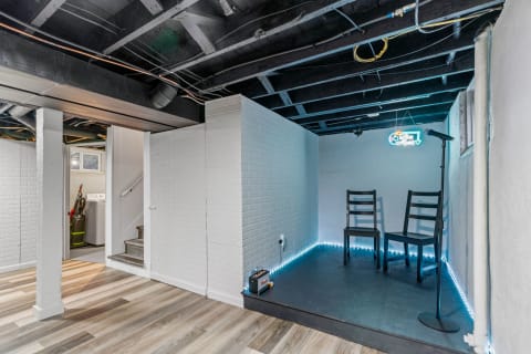 A renovated basement featuring a performance area with black chairs, a microphone, and illuminated edges.