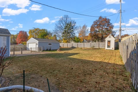 A spacious backyard showcasing autumn colors with a garage and a small shed.