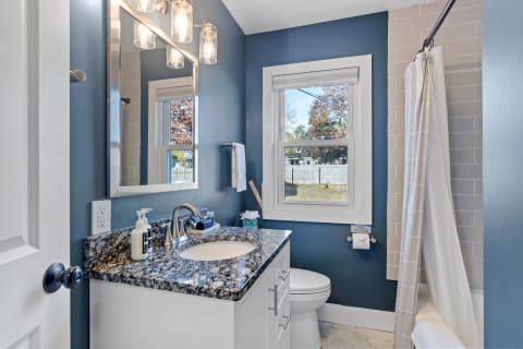 A contemporary bathroom with navy blue walls, granite countertop, and natural light from a window.