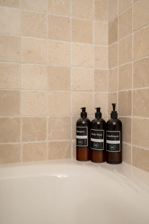 Three neatly arranged bath product bottles in a beige tiled shower corner.