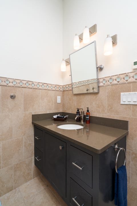 Modern bathroom with dark cabinet, light fixtures, and decorative tiles.