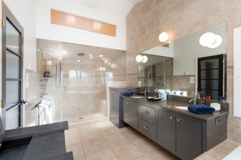 Modern bathroom featuring a glass shower, double vanity, and warm tiled walls.