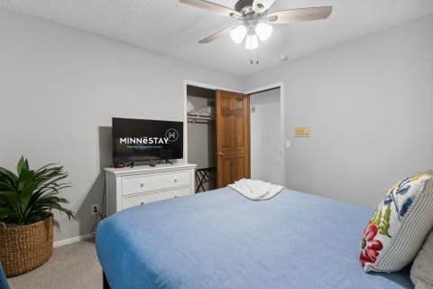 A cozy bedroom featuring a blue bedspread, decorative pillow, and a flat-screen TV on a dresser.