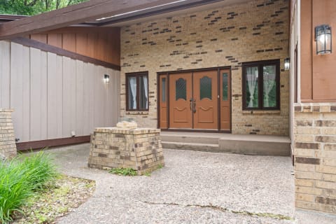 Front entrance of a house with brown double doors, stone details, and greenery.