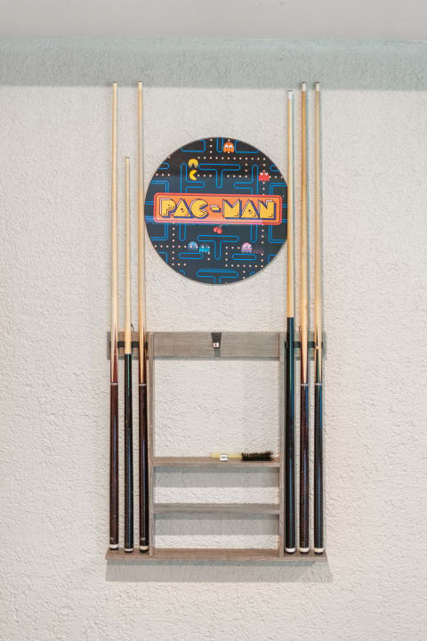 Wall-mounted rack displaying billiard cues and a PAC-MAN logo sign.