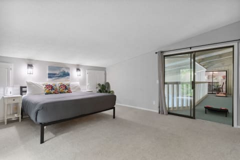 A modern bedroom with a bed, colorful pillows, wall sconces, and a sliding glass door to a balcony.
