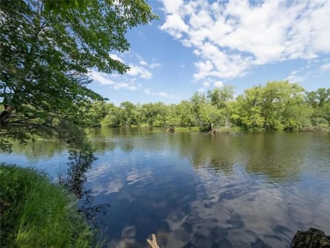 A peaceful river surrounded by green foliage and a blue sky with clouds.