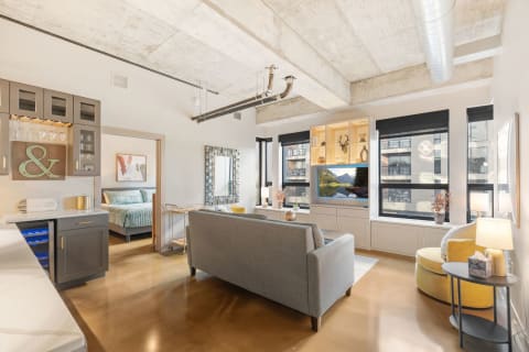 Modern open-concept living space featuring industrial design, a comfortable gray sofa, and a well-equipped kitchen.