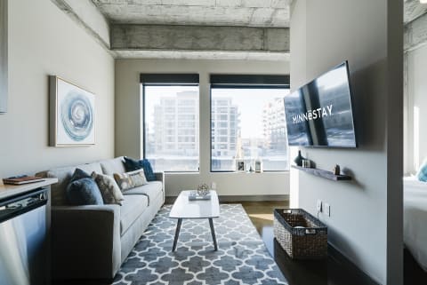 A contemporary apartment living room featuring a gray sofa, a white coffee table, and large windows with an urban view.