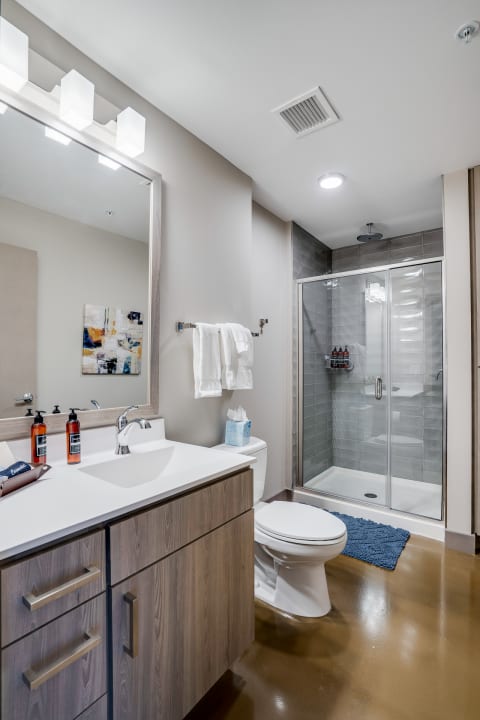 A contemporary bathroom with a light wooden vanity, white countertop, and glass shower enclosure.
