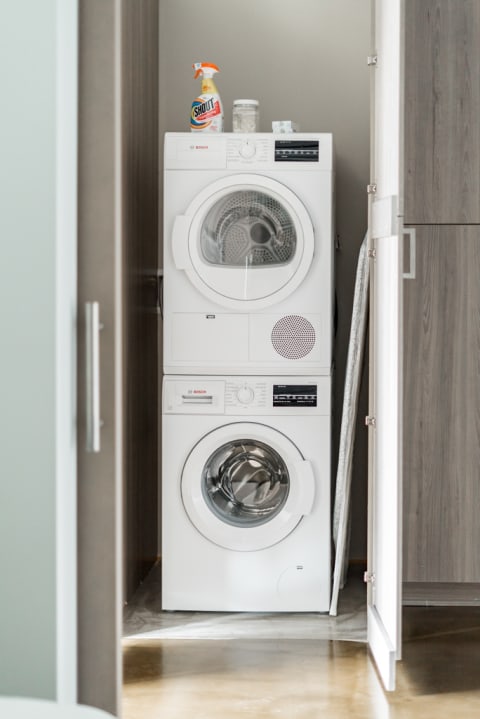 Stacked Bosch washer and dryer with cleaning supplies on top, in a contemporary laundry area.