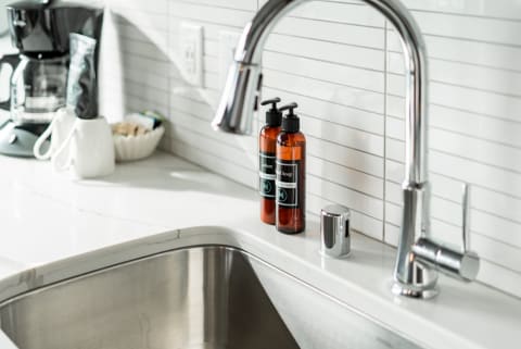 Sleek kitchen sink with amber soap bottles and coffee maker in background.