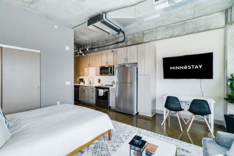 Modern studio apartment showcasing a kitchenette, living area, and bedroom space with minimalist decor.