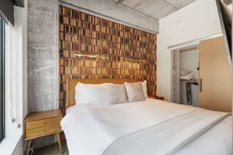 Interior view of a cozy bedroom featuring a bookshelf wallpaper and a wooden bed.