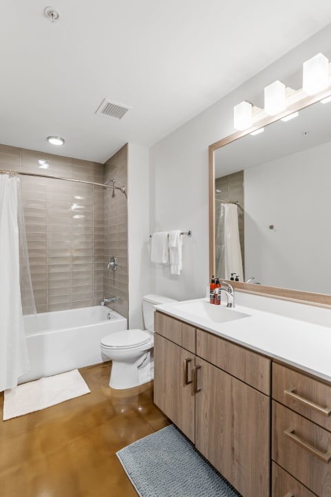 Interior view of a modern bathroom featuring a bathtub, toilet, and wooden vanity.