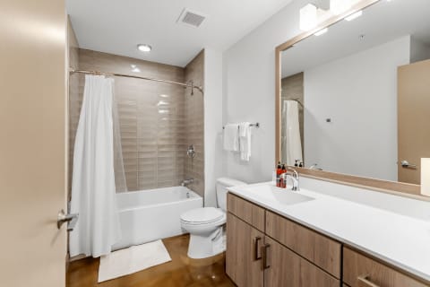 Interior view of a modern bathroom featuring a bathtub, shower curtain, and vanity with a mirror.