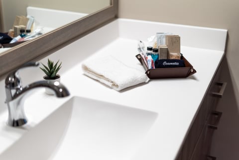 A sleek bathroom countertop with a chrome faucet, a folded towel, a potted plant, and a tray filled with cosmetics.