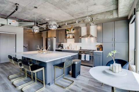 Modern kitchen with gray cabinets, a marble island, and industrial ceiling features.