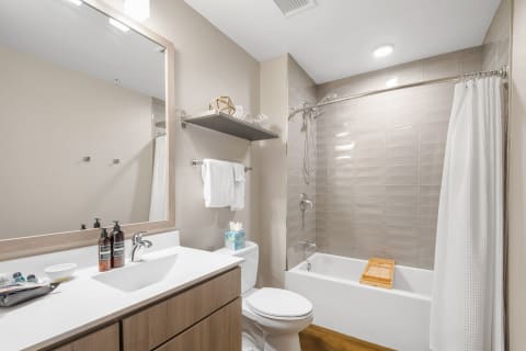 Modern bathroom featuring a white sink, wooden cabinetry, a shower, and a bathtub with a wooden tray.