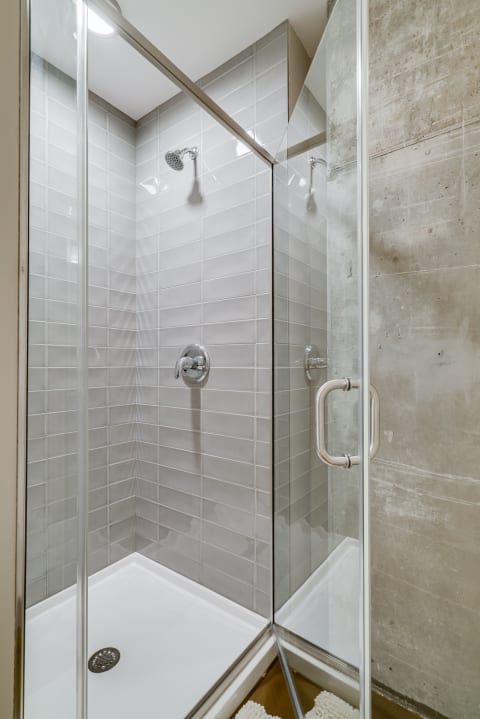 Interior view of a modern shower stall featuring gray tiles and a concrete wall.
