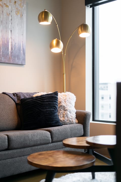 A modern living room featuring a gray sofa with decorative pillows, a gold arch lamp, and wooden coffee tables.