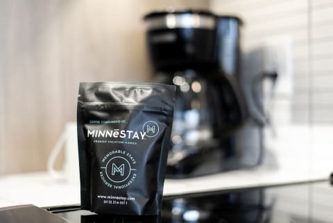 A black coffee bag labeled MINNēSTAY in front of a coffee maker.
