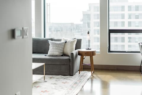 Cozy living room with gray sofa, side table, and natural light from large windows.
