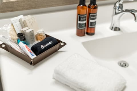 A bathroom countertop with a sink, a tray of cosmetic items, and a washcloth.