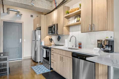 Modern apartment kitchen with light wood cabinets and stainless steel appliances.
