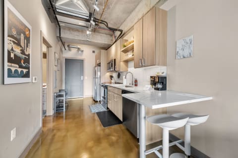 Interior view of a contemporary kitchen with wooden cabinets and stainless steel appliances, featuring a dining bar with stools.