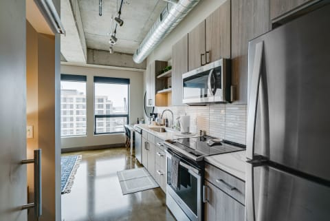 Modern kitchen with stainless steel appliances and large windows showing an urban view.