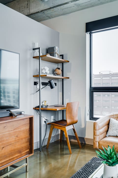 A contemporary workspace with a wooden desk, shelves, and a cozy sofa in an urban setting.
