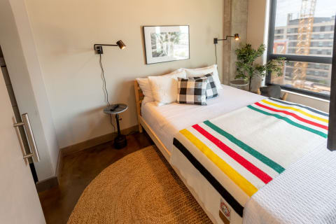 Cozy bedroom featuring a bed with decorative pillows, a colorful throw, and a bedside lamp.